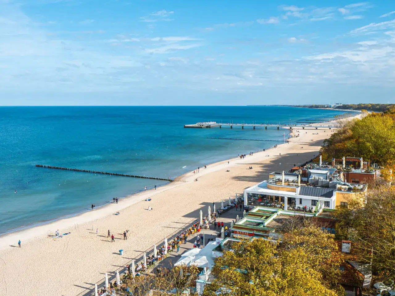 Słoneczna promenada nad morzem tętni życiem. Ludzie spacerują po piaszczystej plaży, a w kawiarniach przy brzegu trwa jesienna sjesta.