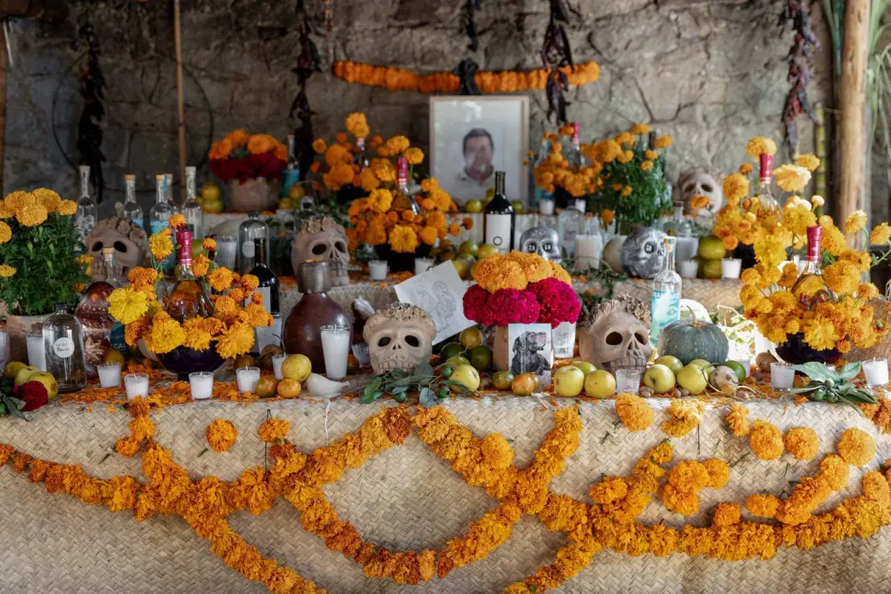 Ołtarz Dia de los Muertos ozdobiony czaszkami, butelkami alkoholu i bujnymi, pomarańczowymi kwiatami.