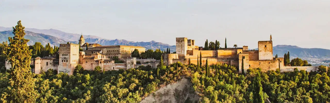 Zabytkowe miasto w Andaluzji, Alhambra, lśni w słońcu. Majestatyczne mury i wieże wznoszą się nad zielonymi wzgórzami.