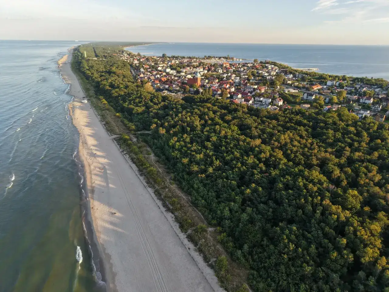 Widok z lotu ptaka na polskie wybrzeże. Długi, piaszczysty brzeg, las i miasteczko. Idealne miejsce, by sprawdzić, ile trwa majówka.