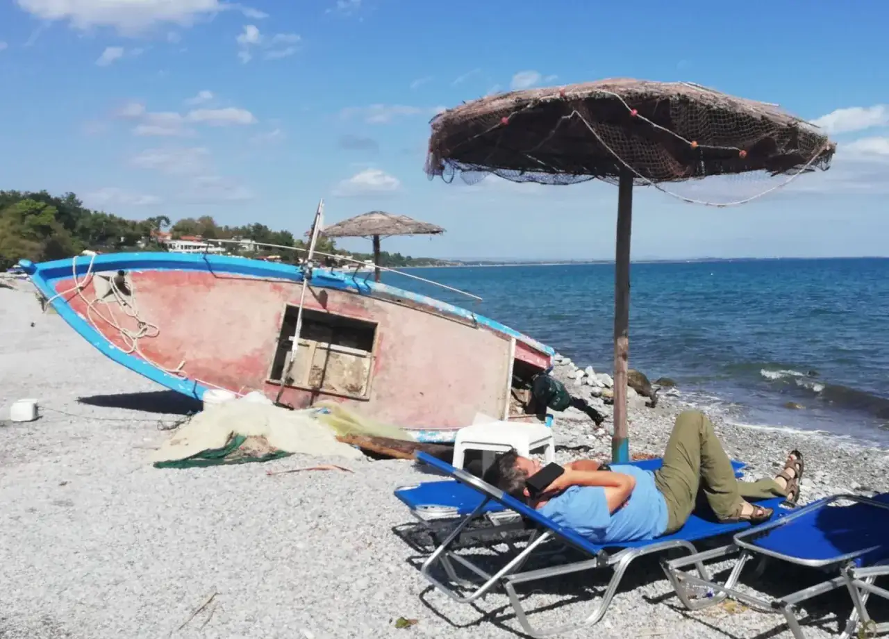 Odpoczynek na plaży Riwiera Olimpijska, obok starej łodzi i parasola.