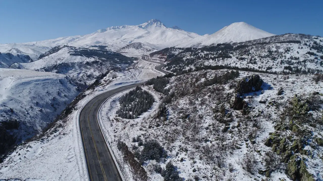 Droga wijąca się przez ośnieżone wzgórza w kierunku majestatycznych gór, zapowiadająca zimowe atrakcje w Erciyes Ski Resort.