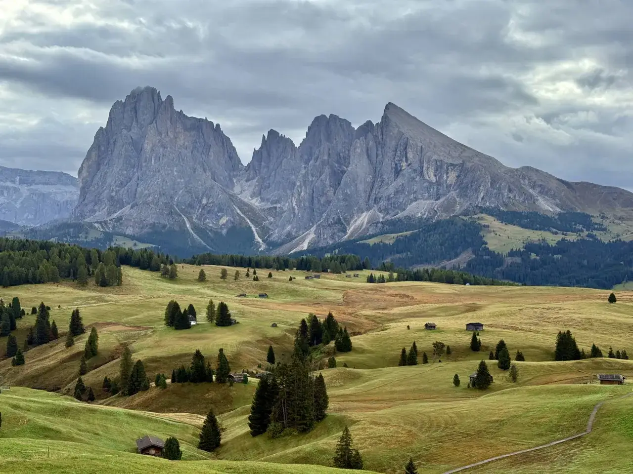 Majestatyczne szczyty Dolomitów, jedne z najpiękniejszych gór w Europie, górują nad zielonymi wzgórzami z maleńkimi chatkami i lasami.