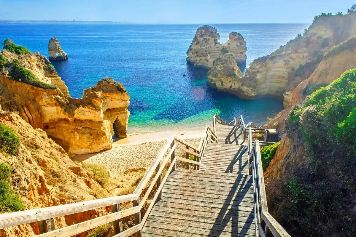 Schody prowadzą do ukrytej plaży z turkusową wodą i skalnymi formacjami. Idealne miejsce, by odkryć, co zobaczyć w Portugalii.