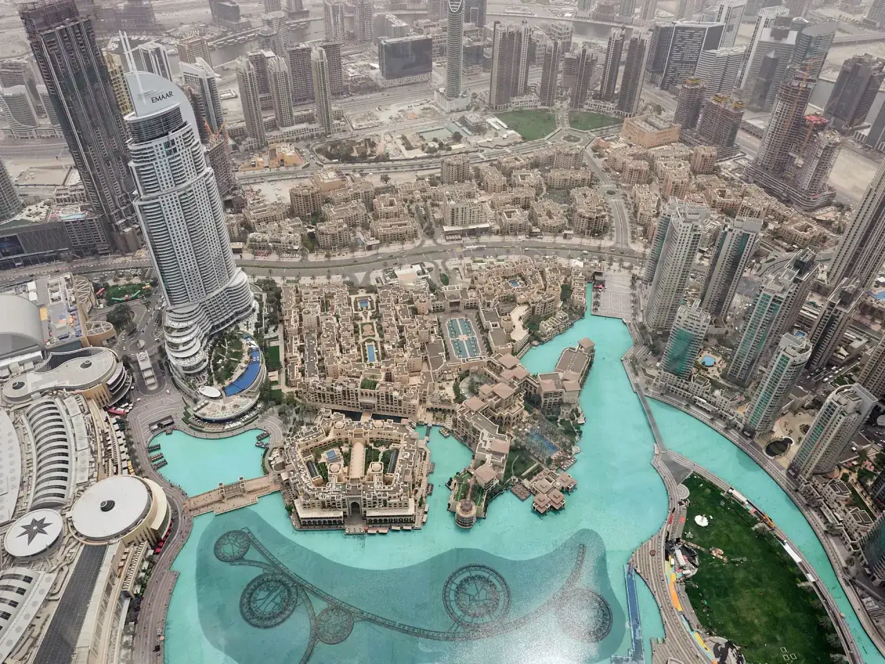 Widok z góry na Dubaj, z najwyższym budynkiem świata w centrum. Widać też wodny plac z fontannami i otaczające go budynki.