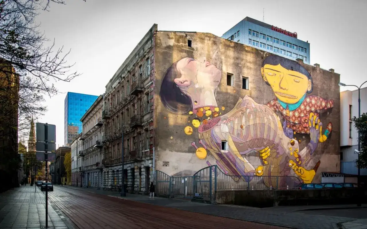 Kolorowe murale w Polsce zdobią miejskie przestrzenie. Na ścianie kamienicy widzimy surrealistyczny obraz z postaciami i elementami anatomicznymi.