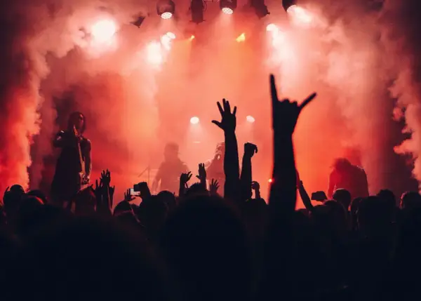 Tłumy na jednym z corocznych festiwali w Polsce, wznoszą ręce w górę, otoczone dymem i czerwonym światłem sceny.