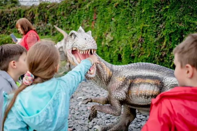 Dzieci w parku rozrywki Zatorland dotykają paszczy dinozaura.