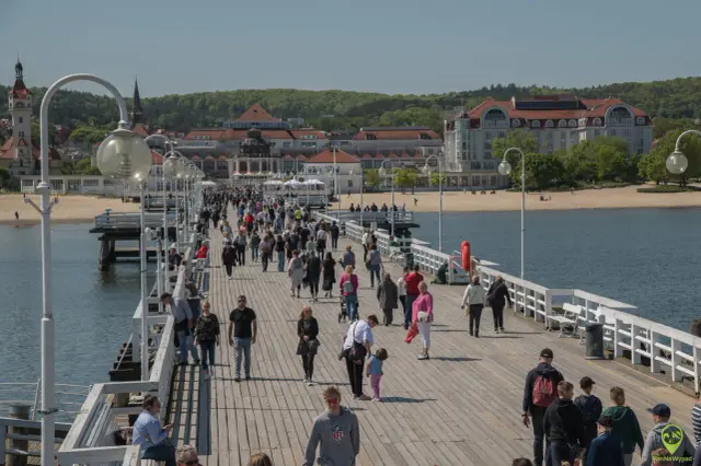 Tłum ludzi spaceruje po molo, podziwiając nadmorskie widoki. To popularne gdańsk atrakcje, idealne na słoneczny dzień.