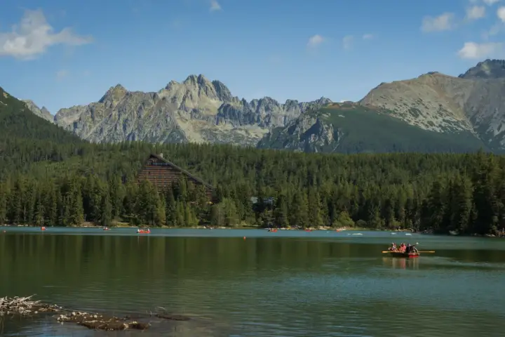 Malownicze jezioro na Słowacji blisko granicy, otoczone lasem i górami. Na wodzie widać łodzie, a w tle hotel w kształcie trójkąta.